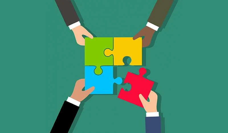 Hands of different people assembling colorful puzzle pieces together.