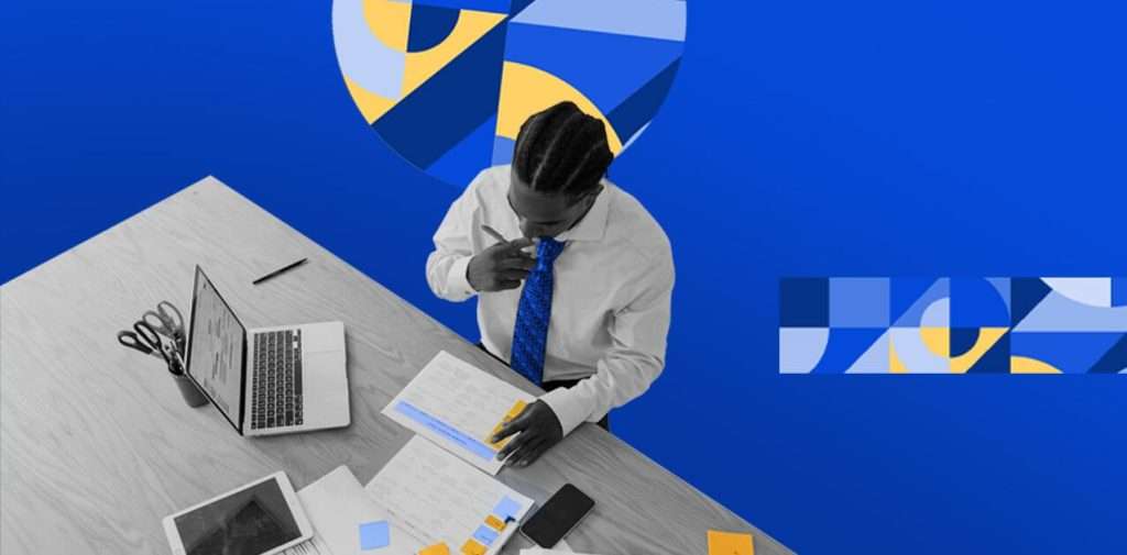 A man in a business attire reviewing documents at a work desk with a laptop, tablet, and smartphone, all in monochrome against a blue background with yellow and blue geometric designs.